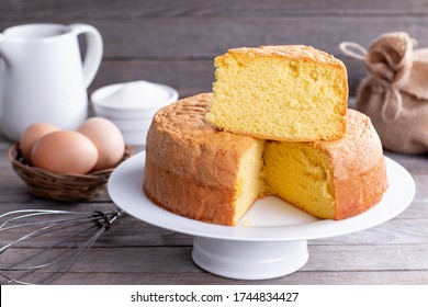 Homemade round sponge cake or chiffon cake on white plate so soft and delicious with ingredients: eggs, flour, milk on wood table. Homemade bakery concept for background and wallpaper.