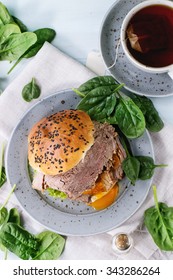 Homemade Sandwich With Baked Meat And Soft-boiled Egg, Spinach Salad, Salt And Cup Of Hot Pocket Tea Over Blue Wooden Table With White Textile. Top View