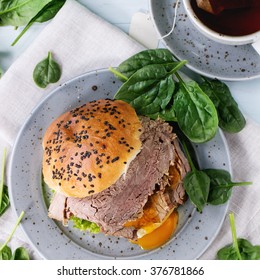 Homemade Sandwich With Baked Meat And Soft-boiled Egg, Spinach Salad, Salt And Cup Of Hot Pocket Tea Over Blue Wooden Table With White Textile. Flat Lay. Square Image