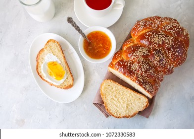 Homemade sesame seed Challah bread, a cup of tea,  orange jam and milk on a white stone background. Top view. 
