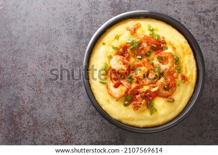 Homemade shrimp and grits with smoked bacon, onions and cheese in a black bowl on a dark concrete background. American cuisine. Horizontal top view from above
