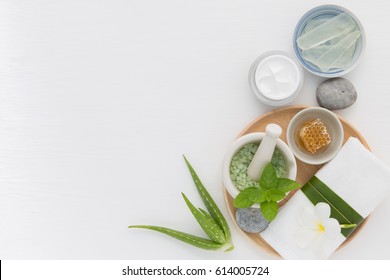 Homemade skin care and body scrub with natural ingredients honey, salt, mint, natural lotion and aloe vera set up on white wooden background.