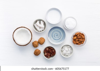 Homemade skin care products on white wooden table background. Coconut, oil, walnut, almond, scrub, milk and lotion from top view. Good for space and background.
