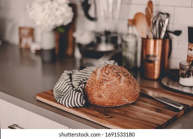 Homemade sourdough bread. Bright white kitchen. Bread on cutting board. Kitchen utensils. Craft authentic bread. Home cooking. Food preparation. Coronavirus covid-19 stay home isolation quarantine. - Powered by Shutterstock