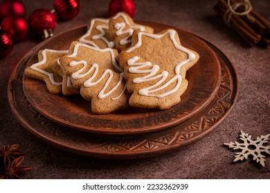 Homemade spiced sweet gingerbread biscuits or crunchy cookies with white sugar icing served on plate on dark brown table with cinnamon, anise and red christmas baubles for new year celebration - Powered by Shutterstock