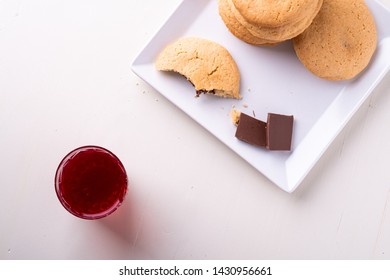 Homemade Stack Of Shortbread Chocolate Cookies With One Bitten Cookie And Two Pieces Of Chocolate On White Plate With Stewed Fruit Red Compote Drink In Glass On Wooden Table Top View