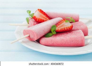 Homemade strawberry ice cream or popsicles in plate on blue wooden table, frozen fruit juice, selective focus.