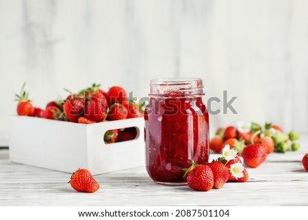 Homemade strawberry preserves or jam in a mason jar surrounded by fresh organic strawberries. Selective focus with blurred foreground and background.