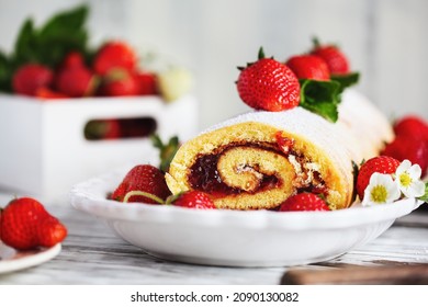 Homemade strawberry shortcake cake roll or Roulade with a berry jam filling and powdered sugar. Dessert over a white rustic wooden table. Selective focus with blurred foreground and background.