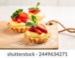 Homemade Strawberry tartlets with vanilla pastry cream - mini fruit tarts filled with custard vanilla pastry cream in a cookie crust. Dessert on awooden board.