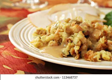 Homemade Stuffing With Gravy Served On Dinner Plate (with Turkey In Background) On Seasonal Tablecloth For Thanksgiving.  Closeup With Shallow Dof.