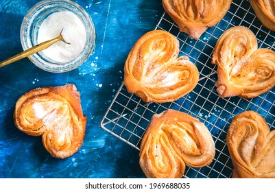 Homemade sugar buns on a cooling rack with sugar for sprinkling. Palmiers, elephant ear, puff pastry cookie. - Powered by Shutterstock