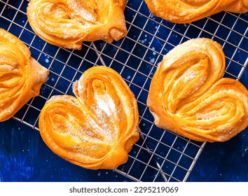 Homemade sugar buns on a cooling rack with sugar for sprinkling. Palmiers, elephant ear, puff pastry cookie. - Powered by Shutterstock