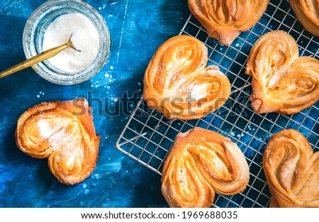 Homemade sugar buns on a cooling rack with sugar for sprinkling. Palmiers, elephant ear, puff pastry cookie.