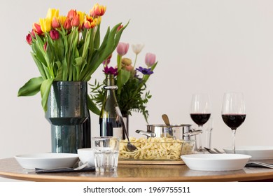 Home-made Swabian Spaetzle (German Spätzle) In Transparent Glass Serving Dish, On A Set Table With Tulips And Other Flowers, And Red Wine Served On Tall Wine Glasses. Small Family Meal For Sunday