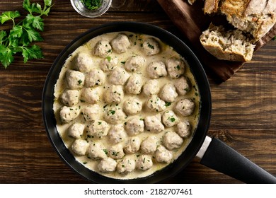 Homemade swedish meatballs with creamy white sauce in cooking pan over wooden background. Top view, lat lay, close up