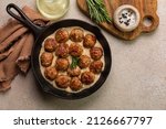 Homemade Swedish Meatballs made with ground meat, onion, egg, bread crumbs and nutmeg, with creamy gravy in a black skillet.  On beige concrete table. Copy space.