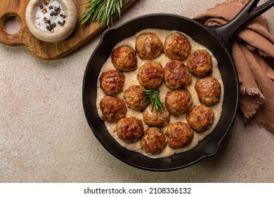 Homemade Swedish Meatballs made with ground meat, onion, egg, bread crumbs and nutmeg. With creamy gravy in black pan skillet.  On beige concrete table.