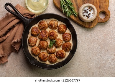 Homemade Swedish Meatballs made with ground meat, onion, egg, bread crumbs and nutmeg, with creamy gravy in a black skillet.  On beige concrete table. Copy space.