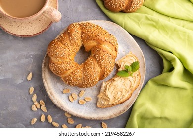 Homemade Sweet Bun With Peanut Butter And Cup Of Coffee On A Gray Concrete Background And Green Linen Textile. Top View, Flat Lay, Close Up.