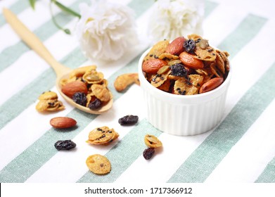 Homemade sweet caramel cereal cornflakes with mixed nut, almonds, raisins,cashews and pumpkin seeds in white bowl with wooden spoon on  the table background, Caramel Snack Mix Recipe