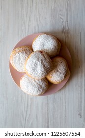 Homemade sweet donuts with powdered sugar on pink plate on white wooden background, top view. Flat lay, overhead, from above.
