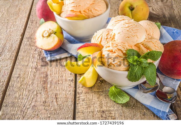 Homemade\
sweet peach ice cream. Peach gelato balls in small bowls, on wooden\
background with fresh peaches and mint\
leaves