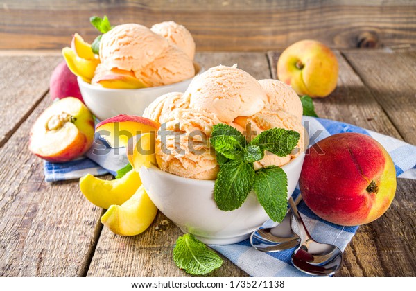 Homemade\
sweet peach ice cream. Peach gelato balls in small bowls, on wooden\
background with fresh peaches and mint\
leaves