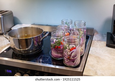 Homemade sweet and spicy pickled red onions sliced in a large mason glass jar, made with chilli peppers, garlic, pepper corns, rosemary and apple cider vinegar. Sitting on a stove top.  - Powered by Shutterstock