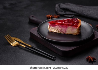 Homemade tasty cheesecake with jelly and raspberry berries on a black plate on a dark concrete background