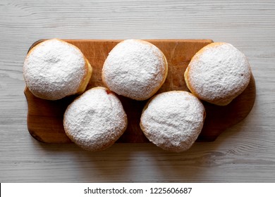 Homemade tasty donuts with jelly and powdered sugar on rustic wooden board over white wooden background, top view. Close-up.