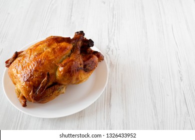 Homemade Tasty Rotisserie Chicken On White Plate Over White Wooden Background, Low Angle View. Copy Space.