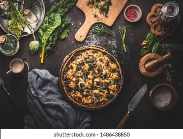 Homemade tasty salmon open faced pie or quiche lorraine on dark rustic table background with kitchen utensils and ingredients, top view