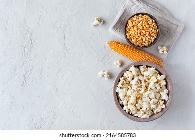 Homemade tasty traditional popcorn, raw corn seeds and corncob on concrete background. The top view with copy space