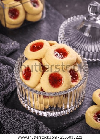 Homemade thumb print cookies filled with strawberry jam on bowl. High angle view. Selective focus
