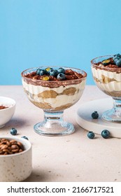 Homemade Tiramisu With Blueberries In Glass Jars. Traditional Unbaked Italian Dessert On Blue Background. Coffee And Mascarpone Cream Cake. Copy Space. Selective Focus.