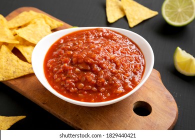 Homemade Tomato Salsa And Nachos On A Rustic Wooden Board On A Black Surface, Side View. Close-up.