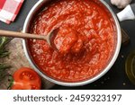 Homemade tomato sauce and spoon in pot on dark table, flat lay