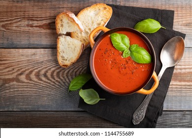Homemade tomato soup with Basil, toast and olive oil on a wooden table. Prepared a vegetarian dish on a dark background. Top view with copy space