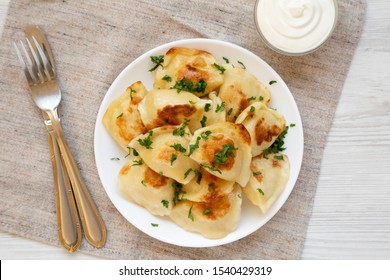 Homemade Traditional Polish Fried Potato Pierogis On A White Plate With Sour Cream, Overhead View. Top View, From Above, Flat Lay. Closeup.