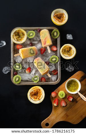 Homemade tropical ice cream or popsicles garnished with pieces of ice and passion fruit, kiwi, grapes and strawberries, top view