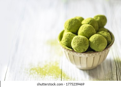 Homemade truffle sweets with green matcha tea in a ceramic bowl on a light wooden background. Raw energy balls. Selective focus, copy space