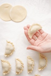 Homemade Ukrainian Varenyki. A Hand Holds A Raw Dumpling On The Background Of The Cooking Process, Raw Dumplings And Circles Of Dough