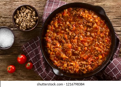 Homemade vegan bolognese sauce made with soy meat, fresh tomatoes, onion and garlic, served in cast iron skillet, photographed overhead on rustic wood