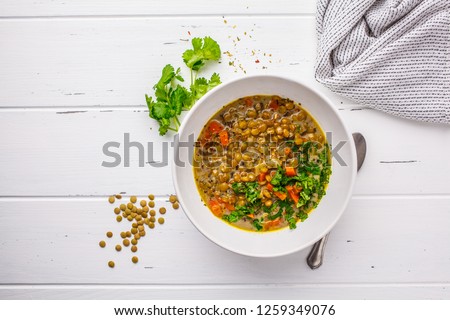Homemade vegan lentil soup with vegetables and cilantro, white wooden background, top view. Indian vegetarian cuisine.