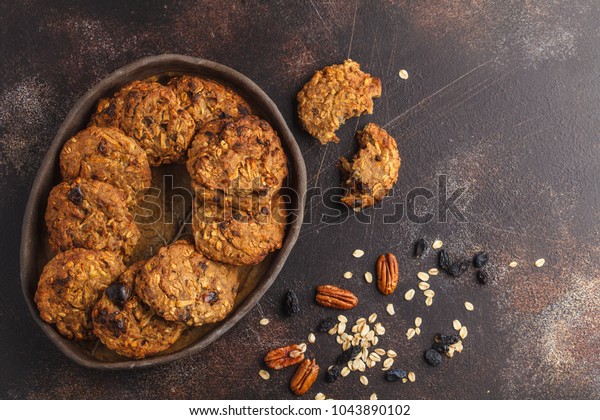 Homemade vegan oatmeal cookies with raisins,\
pecans and dates. Healthy vegetarian dessert concept. Dark rusty\
background, copy\
space.