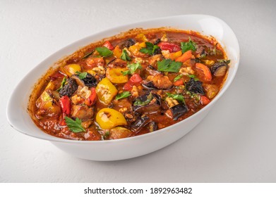 Homemade vegetable stew of eggplant, zucchini, tomatoes, peppers, garlic, prunes and greens on bowl on light background. Close up