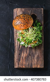 Homemade Veggie Sweet Potato Burger With Fresh Radish And Pea Sprouts Served On Wooden Chopping Board Over Black Textured Background. Top View