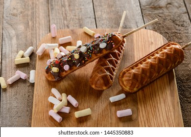 Homemade waffle lollies on a cutting board. Tasty dessert on a skewer, topped with chocolate, marshmallow and sprinkles.