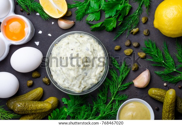 Homemade white sauce\
tartar tartare with ingredients pickles, capers, dill, parsley,\
garlic, lemon and mustard on a dark black stone concrete\
background. Horizontal, top\
view